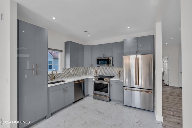 kitchen featuring tasteful backsplash, gray cabinetry, sink, and appliances with stainless steel finishes