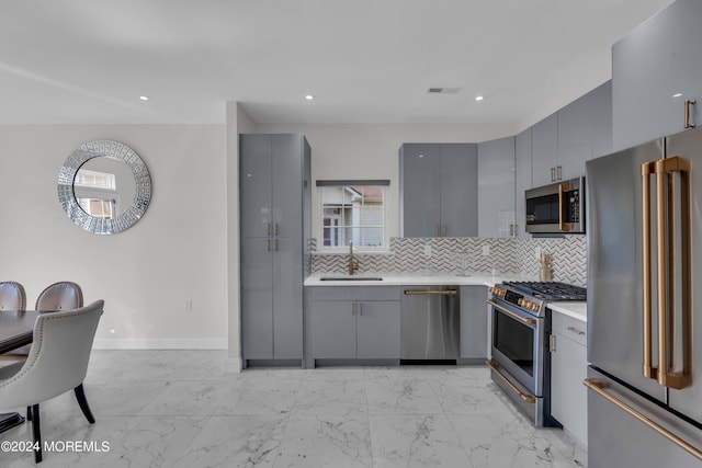 kitchen with gray cabinets, decorative backsplash, sink, and high end appliances