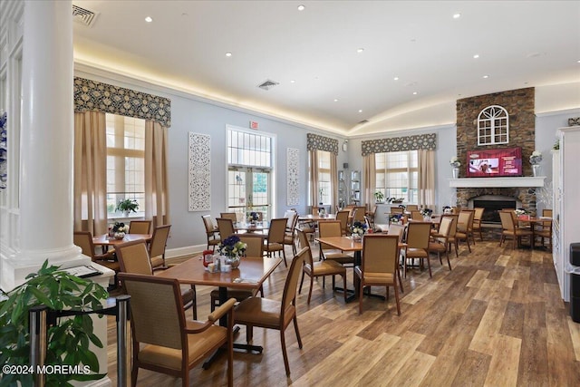 dining space featuring hardwood / wood-style floors, lofted ceiling, a fireplace, plenty of natural light, and decorative columns