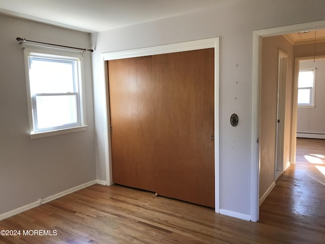 unfurnished bedroom featuring multiple windows, a closet, a baseboard heating unit, and light wood-type flooring