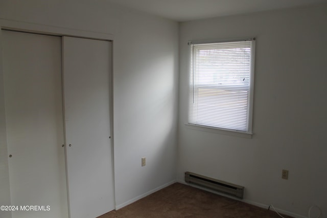 unfurnished bedroom featuring carpet flooring, a closet, and a baseboard heating unit