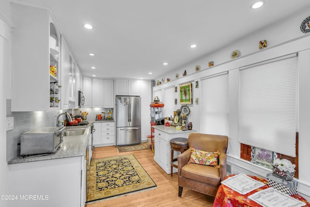 kitchen featuring appliances with stainless steel finishes, tasteful backsplash, sink, light hardwood / wood-style flooring, and white cabinetry