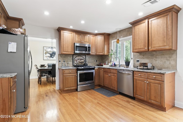 kitchen with light stone countertops, backsplash, stainless steel appliances, pendant lighting, and light hardwood / wood-style floors