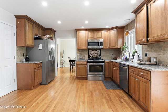 kitchen featuring light stone countertops, pendant lighting, stainless steel appliances, and light hardwood / wood-style floors