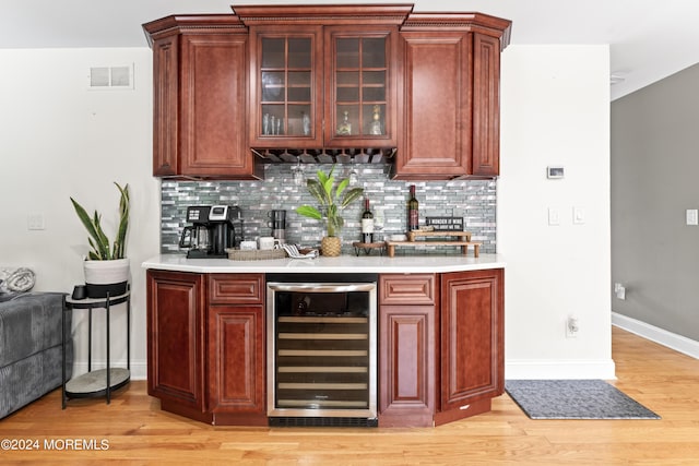 bar featuring light wood-type flooring, backsplash, and beverage cooler