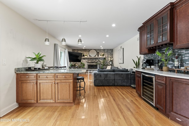 kitchen featuring hanging light fixtures, a kitchen breakfast bar, wine cooler, light hardwood / wood-style flooring, and a fireplace