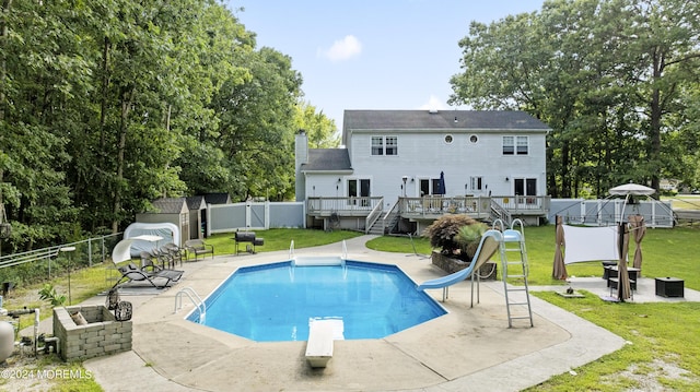 view of swimming pool with a lawn, a water slide, a wooden deck, and a diving board