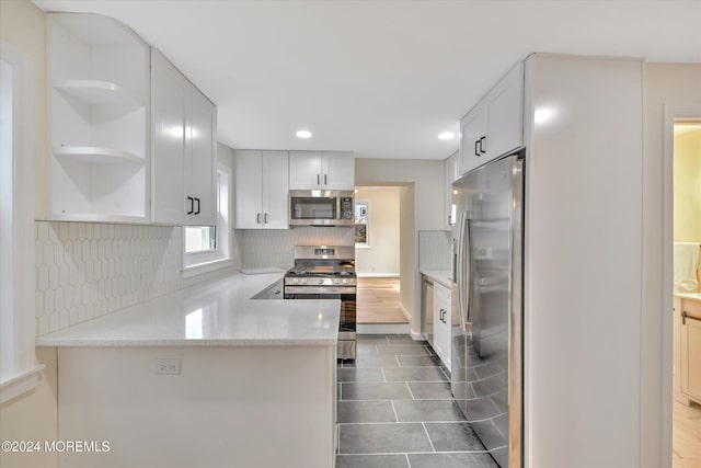 kitchen with kitchen peninsula, light stone counters, white cabinetry, and stainless steel appliances