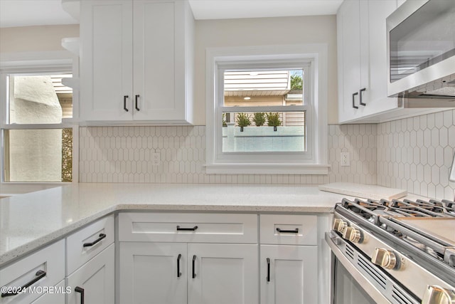 kitchen with white cabinets, backsplash, light stone countertops, and stainless steel range oven