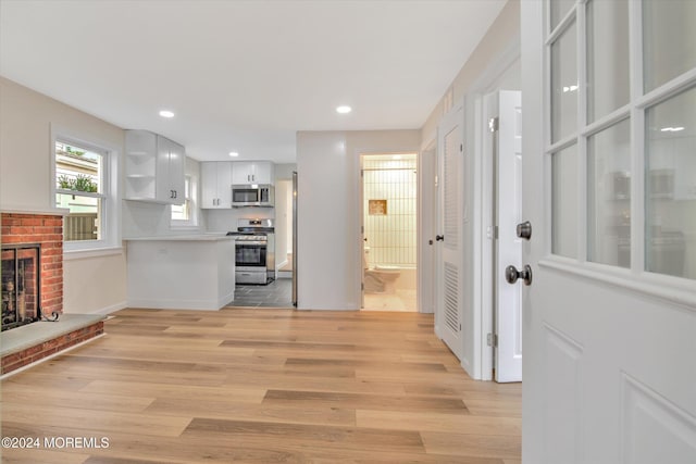 interior space featuring backsplash, stainless steel appliances, a fireplace, light hardwood / wood-style floors, and white cabinetry