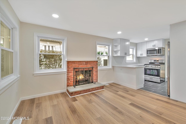 kitchen with stainless steel appliances, a brick fireplace, tasteful backsplash, light hardwood / wood-style floors, and white cabinets