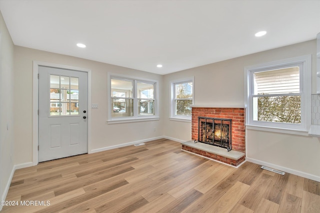 unfurnished living room featuring plenty of natural light, light hardwood / wood-style floors, and a brick fireplace