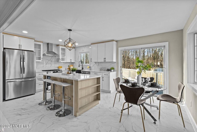 kitchen with wall chimney exhaust hood, stainless steel appliances, decorative light fixtures, white cabinets, and a kitchen island