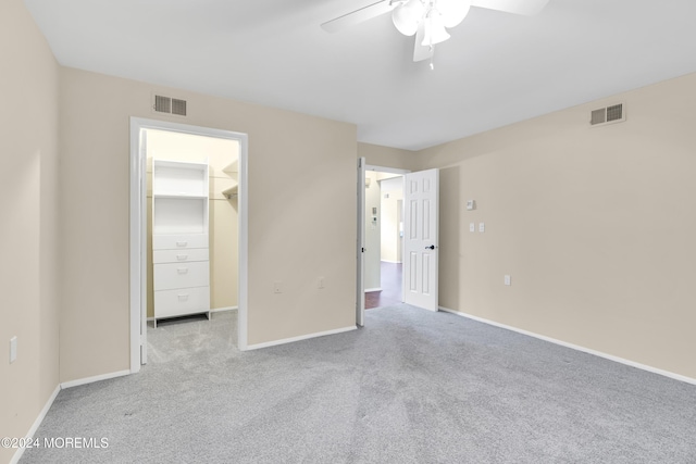 unfurnished bedroom with a closet, a spacious closet, ceiling fan, and light colored carpet