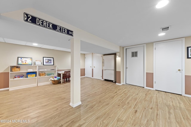 basement featuring white refrigerator and light hardwood / wood-style flooring