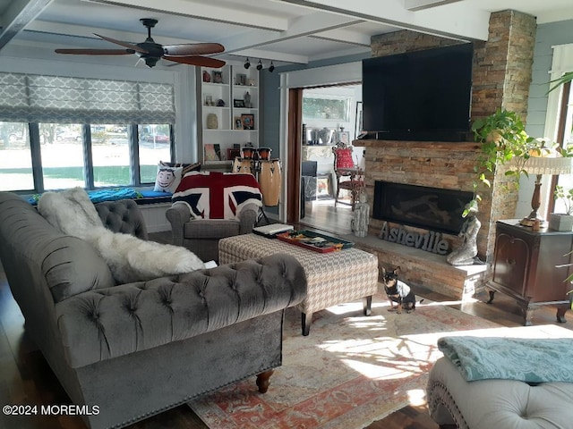 living room with a stone fireplace, ceiling fan, beamed ceiling, and hardwood / wood-style flooring