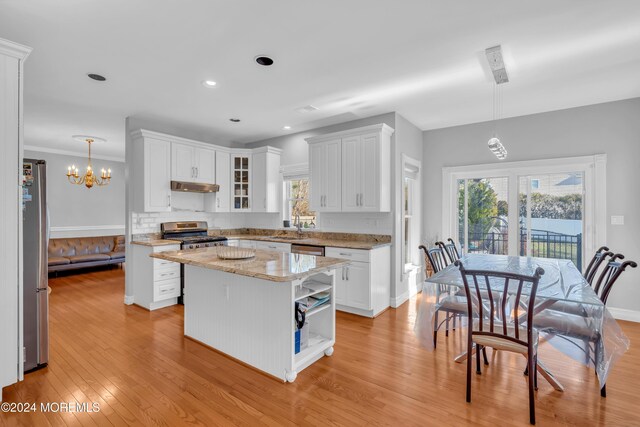 kitchen with light wood-type flooring, stainless steel appliances, a center island, white cabinetry, and hanging light fixtures