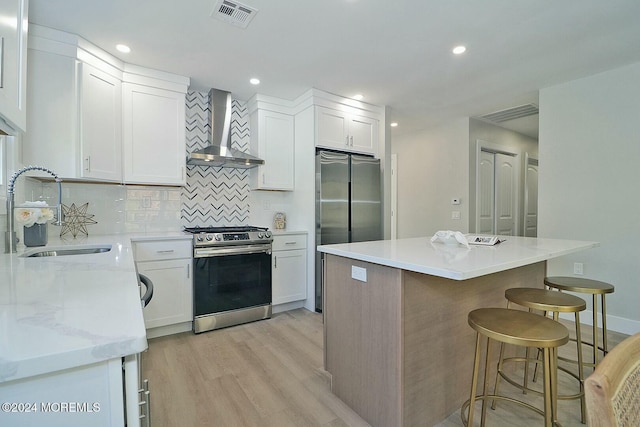 kitchen with sink, wall chimney range hood, light hardwood / wood-style flooring, white cabinets, and appliances with stainless steel finishes