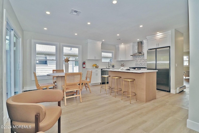 kitchen with a center island, a baseboard heating unit, white cabinets, wall chimney exhaust hood, and stainless steel appliances