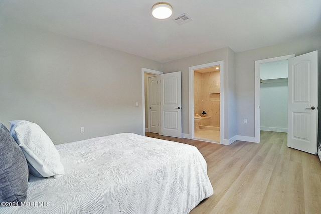 bedroom featuring light wood-type flooring, connected bathroom, a spacious closet, and a closet