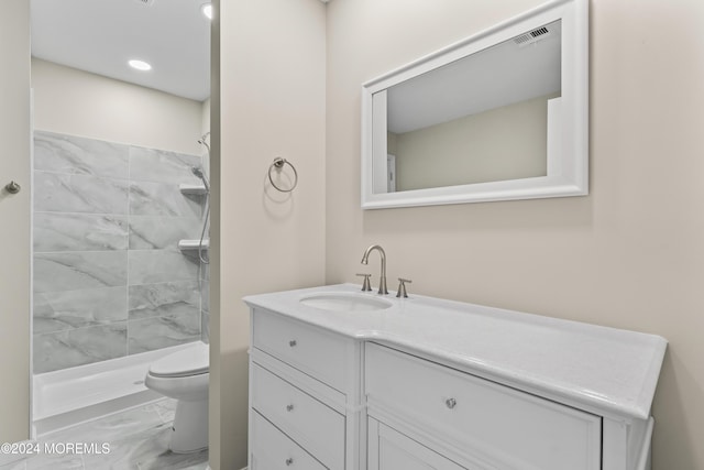 bathroom with tiled shower, vanity, and toilet