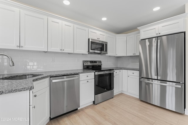 kitchen with white cabinets, sink, dark stone countertops, light hardwood / wood-style floors, and stainless steel appliances