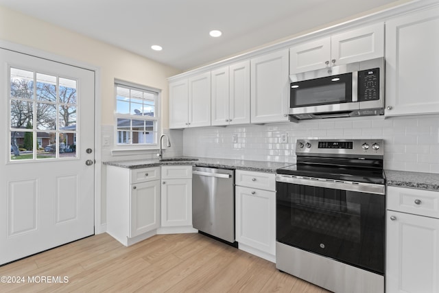 kitchen featuring sink, dark stone counters, light hardwood / wood-style floors, white cabinets, and appliances with stainless steel finishes