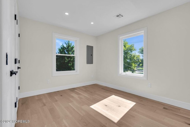 spare room featuring electric panel and light hardwood / wood-style floors