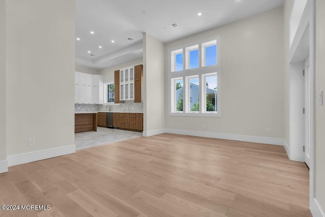 unfurnished living room with sink, a towering ceiling, and light hardwood / wood-style floors