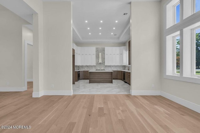 kitchen featuring dark brown cabinetry, white cabinetry, wall chimney range hood, a raised ceiling, and light wood-type flooring