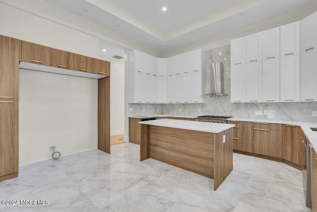 kitchen with a center island, wall chimney exhaust hood, tasteful backsplash, white cabinetry, and stainless steel gas cooktop