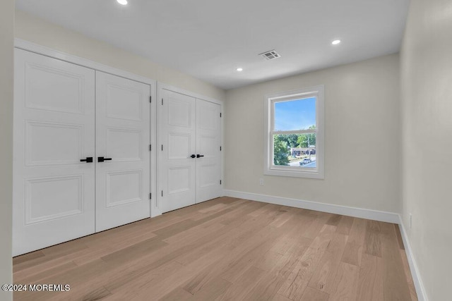 unfurnished bedroom with light wood-type flooring and multiple closets