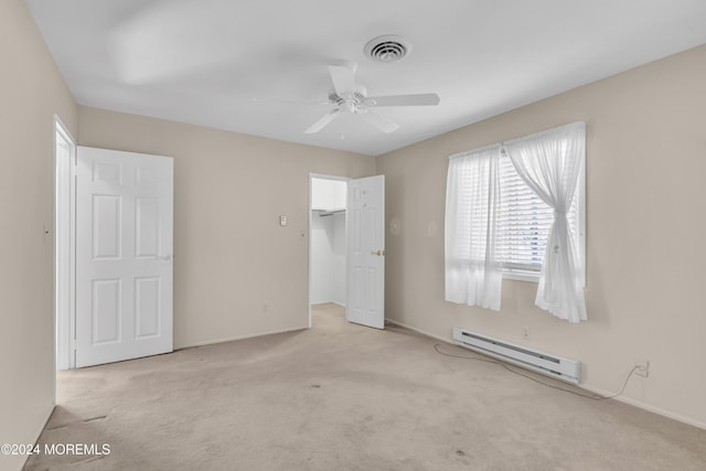 unfurnished bedroom with a walk in closet, light colored carpet, ceiling fan, a baseboard heating unit, and a closet