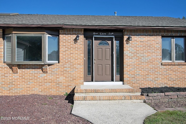 view of exterior entry featuring roof with shingles and brick siding