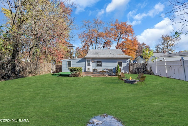 rear view of property featuring a lawn, an outdoor living space with a fire pit, and a deck