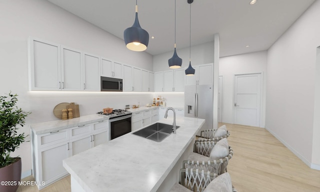 kitchen featuring a kitchen island with sink, sink, appliances with stainless steel finishes, decorative light fixtures, and white cabinetry