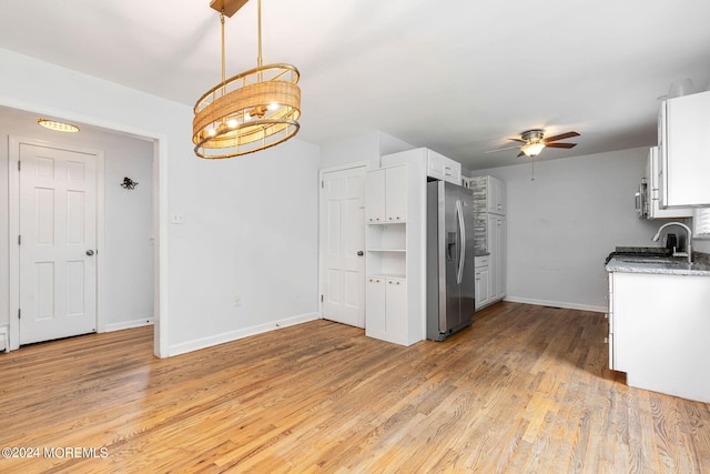 kitchen featuring stainless steel fridge, light wood-type flooring, ceiling fan with notable chandelier, decorative light fixtures, and white cabinetry