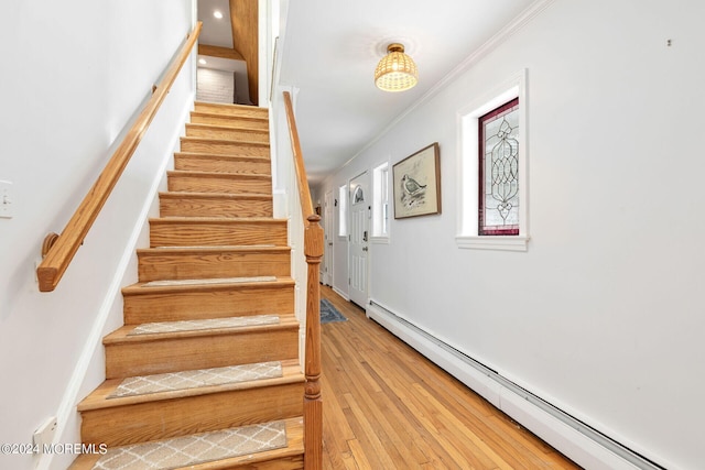 stairway featuring baseboard heating, ornamental molding, and hardwood / wood-style flooring