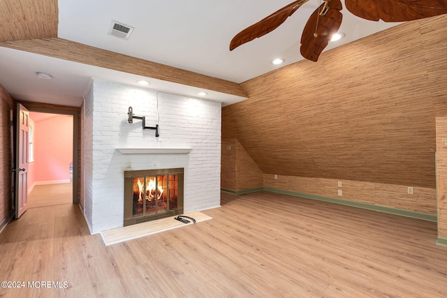 unfurnished living room featuring wood walls, light wood-type flooring, vaulted ceiling, and a brick fireplace