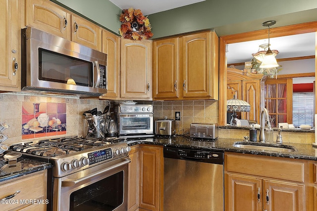 kitchen featuring decorative backsplash, appliances with stainless steel finishes, sink, dark stone countertops, and hanging light fixtures