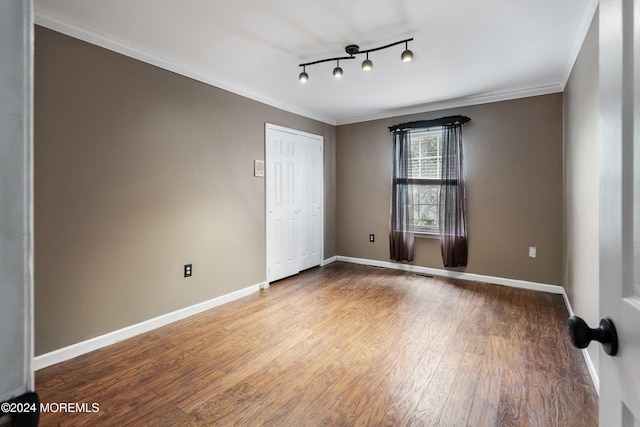 empty room with ornamental molding, track lighting, and hardwood / wood-style flooring