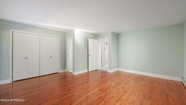 unfurnished bedroom featuring light hardwood / wood-style floors, a closet, and a baseboard heating unit