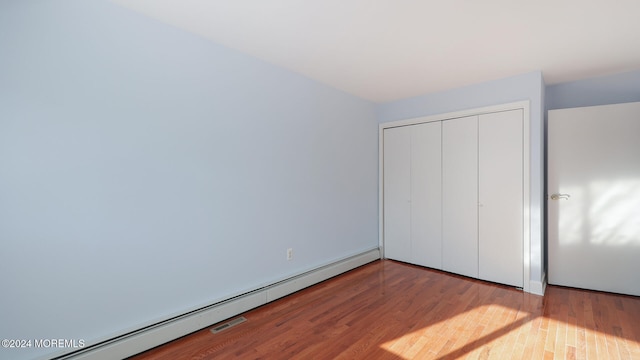 unfurnished bedroom with light wood-type flooring, a closet, and baseboard heating