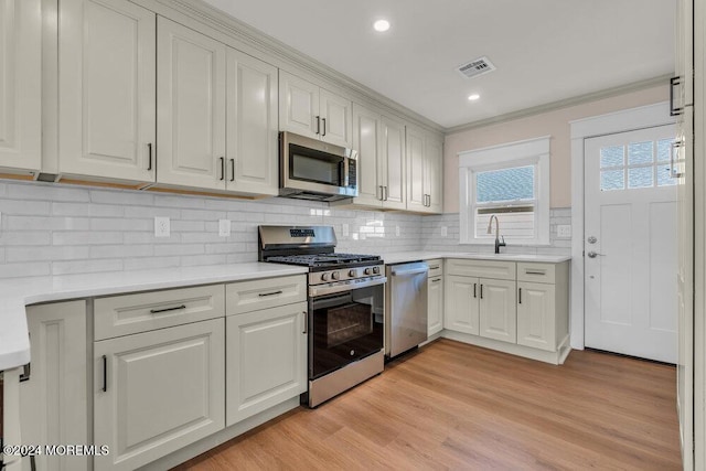 kitchen with stainless steel appliances, white cabinetry, sink, and light hardwood / wood-style floors