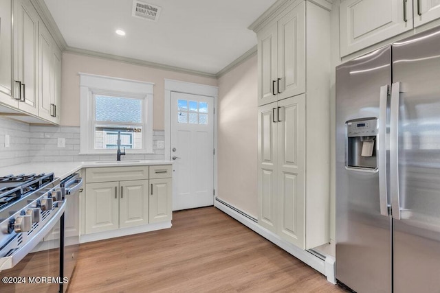 kitchen featuring appliances with stainless steel finishes, tasteful backsplash, a baseboard radiator, sink, and white cabinets