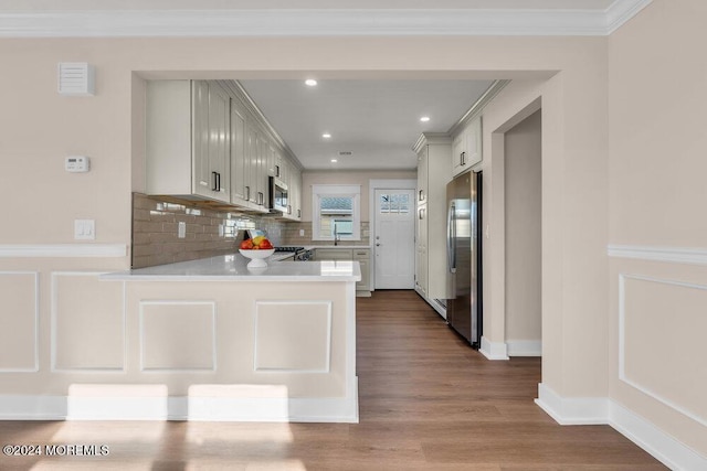 kitchen with tasteful backsplash, hardwood / wood-style flooring, ornamental molding, kitchen peninsula, and stainless steel appliances