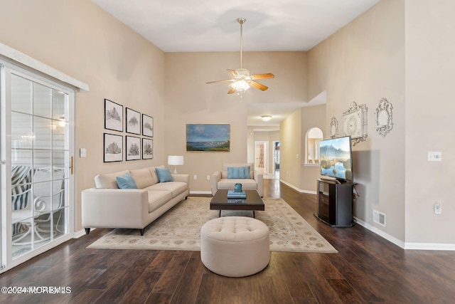 living room with ceiling fan, a towering ceiling, and dark wood-type flooring