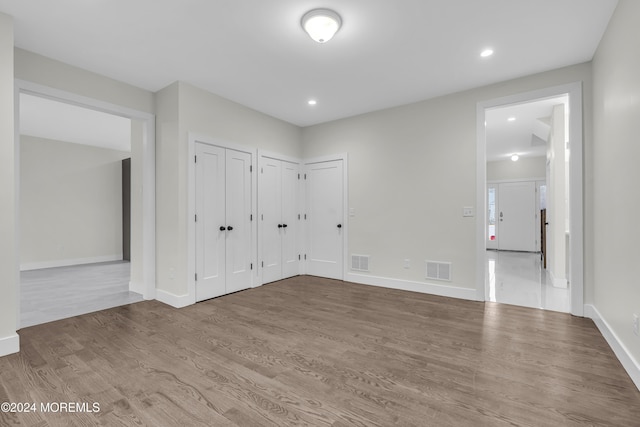 unfurnished bedroom with hardwood / wood-style floors and multiple closets