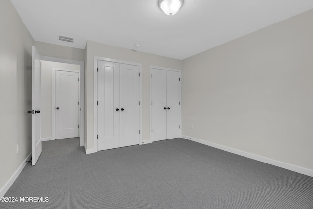 unfurnished bedroom with two closets and dark colored carpet