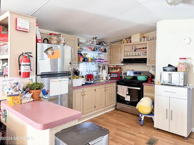 kitchen featuring sink, stainless steel appliances, cream cabinets, light hardwood / wood-style floors, and vaulted ceiling